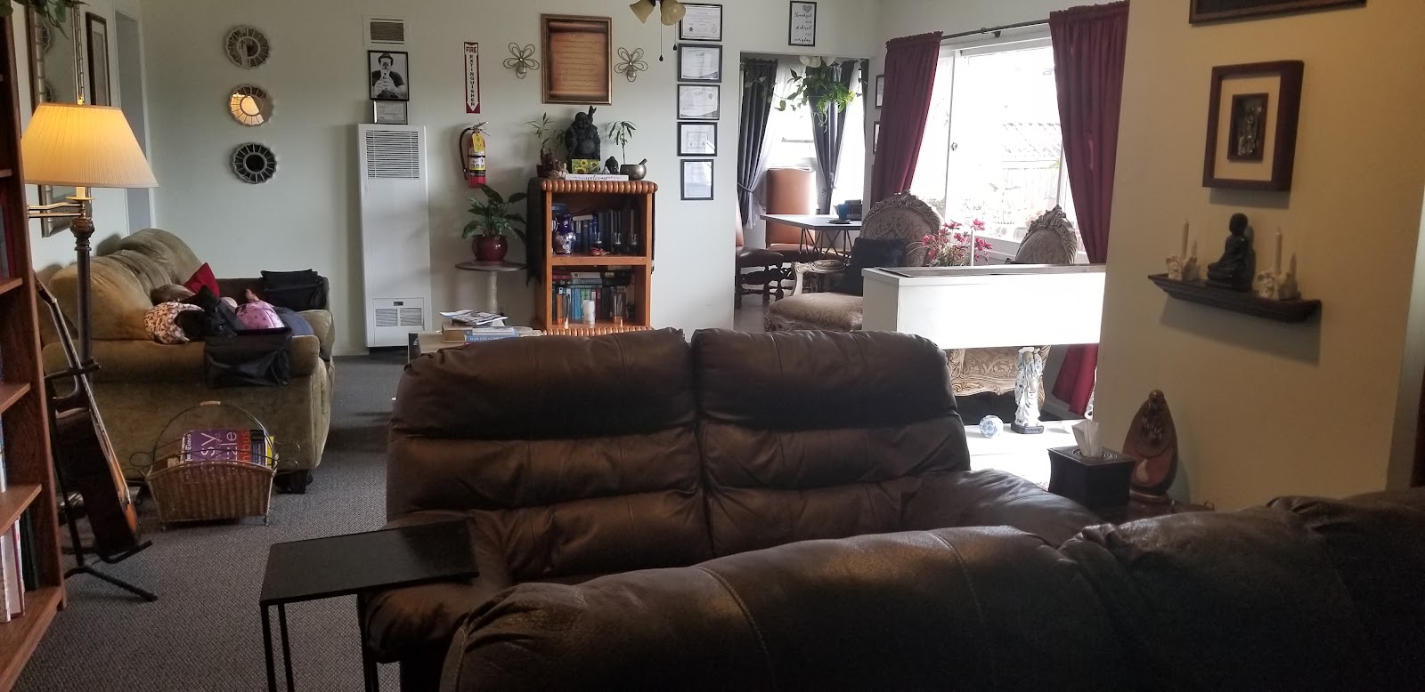 Interior common area with brown leather sectional sofa, armchair, wooden bookshelf, wall decor, and large windows with curtains
