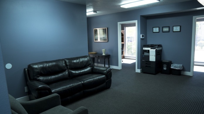 Interior lounge with black leather sofa, glass door entry, office equipment, and windows with exterior view