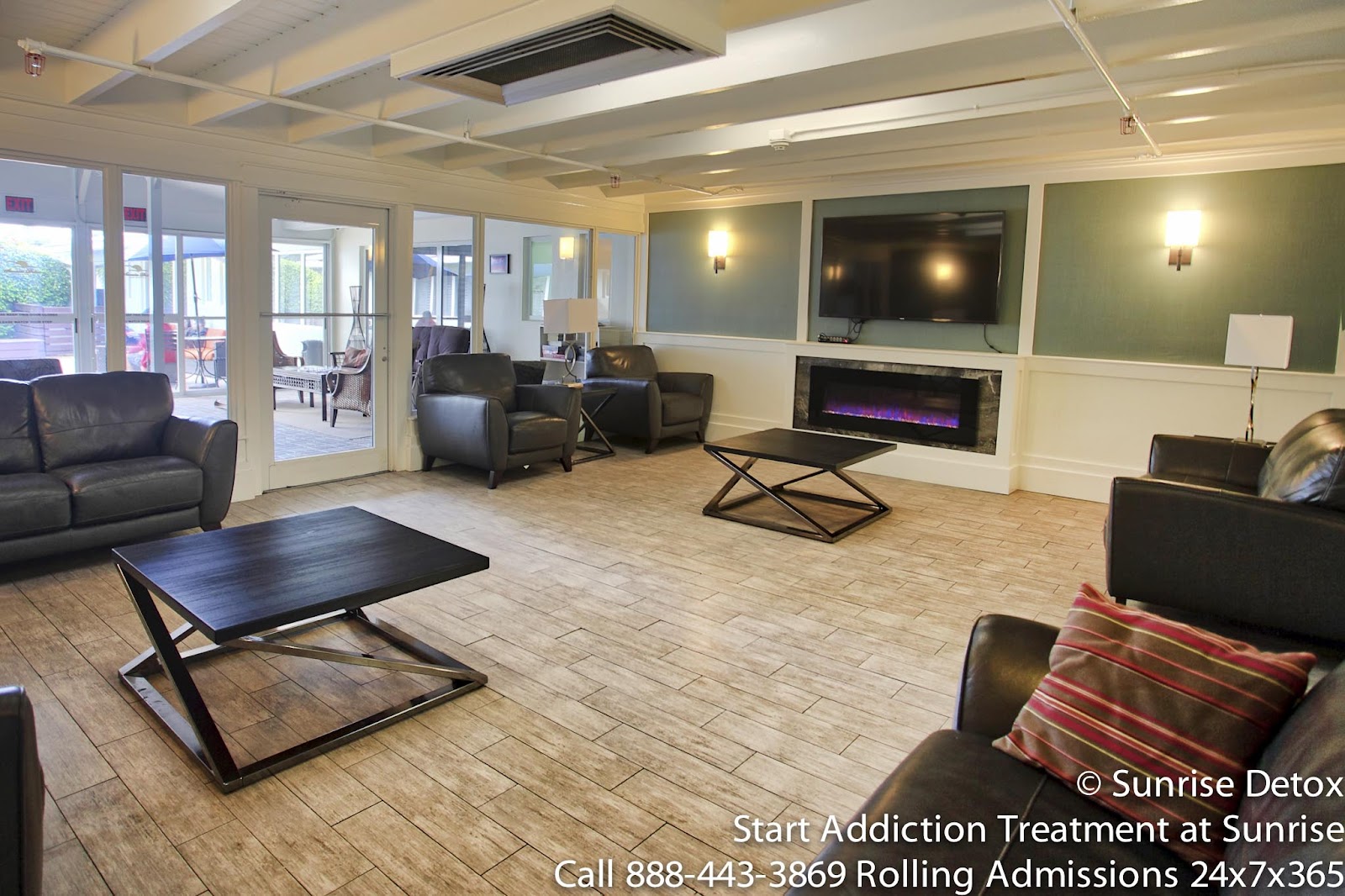 Interior common area with black leather seating, glass doors, mounted flat-screen television, fireplace, and wood flooring.