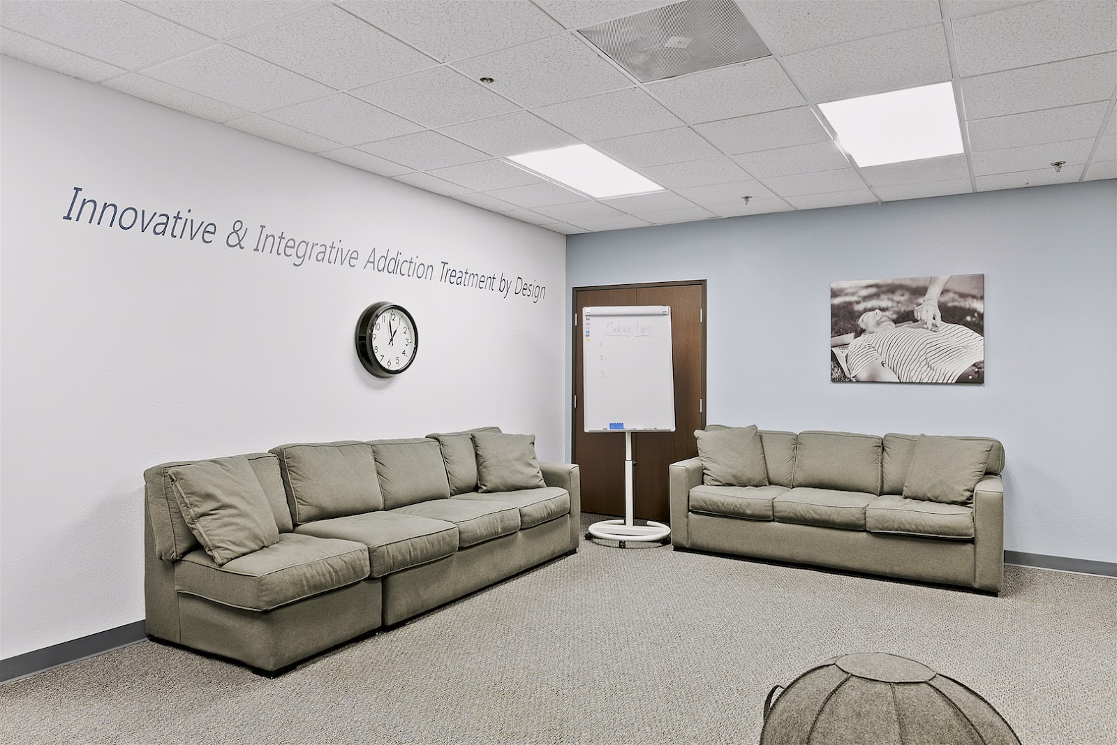 Interior common lounge area with two beige couches, clock, wall signage, and treatment photography