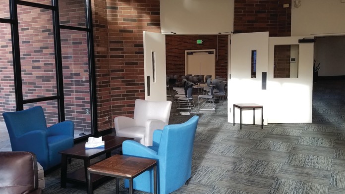 Interior common area with blue armchairs, white accent chair, dark tables, exposed brick walls, and group meeting area