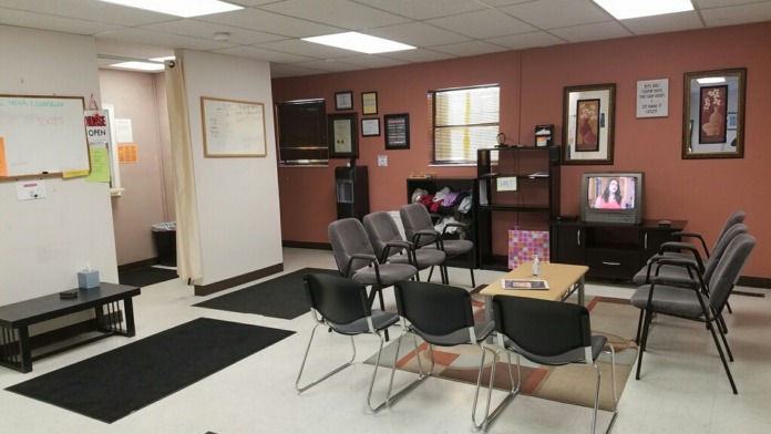 Interior common area with multiple chairs, tables, television, and orange accent walls for patient gathering