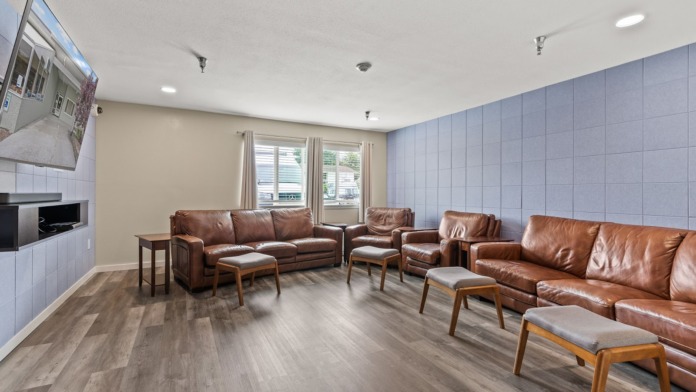 Interior common area with brown leather sectional sofa, armchairs, fireplace, mounted television, light blue walls, and wood flooring