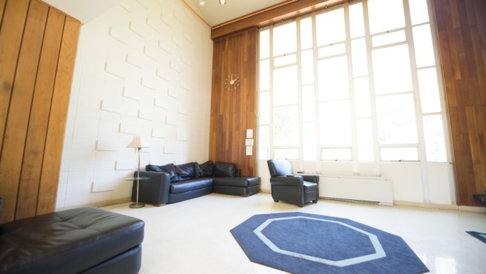 Spacious interior room with white brick walls, dark leather sectional, geometric rug, and glass doors