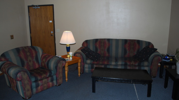 Interior common area with striped upholstered sofa and armchair, table lamp, coffee table, and door to adjacent room