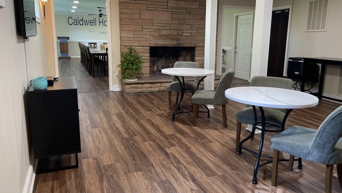Interior common area with wooden dining tables, brick fireplace, lounge seating, and wood flooring throughout