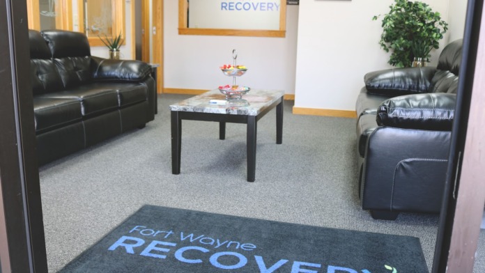 Interior lounge with leather seating, coffee table, potted plant, and Fort Wayne Recovery branding on walls