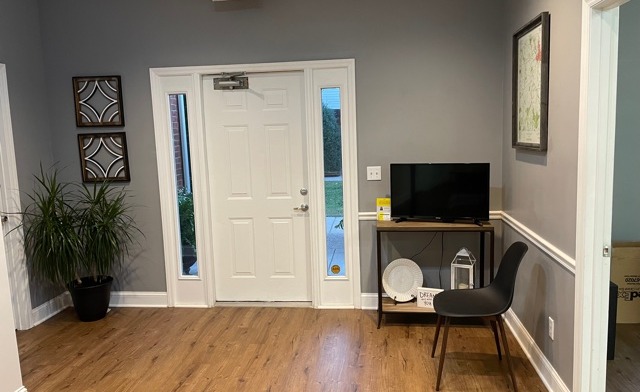 Interior lounge with gray walls, wooden flooring, television, chair seating, and exit sign overhead