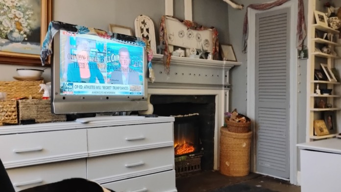 Interior common area featuring electric fireplace, television, white cabinetry, shelving with decorative items, and comfortable seating