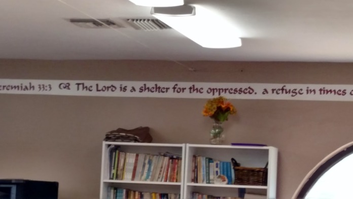 Interior common space with bookshelves, biblical verse wall text, and decorative flowers