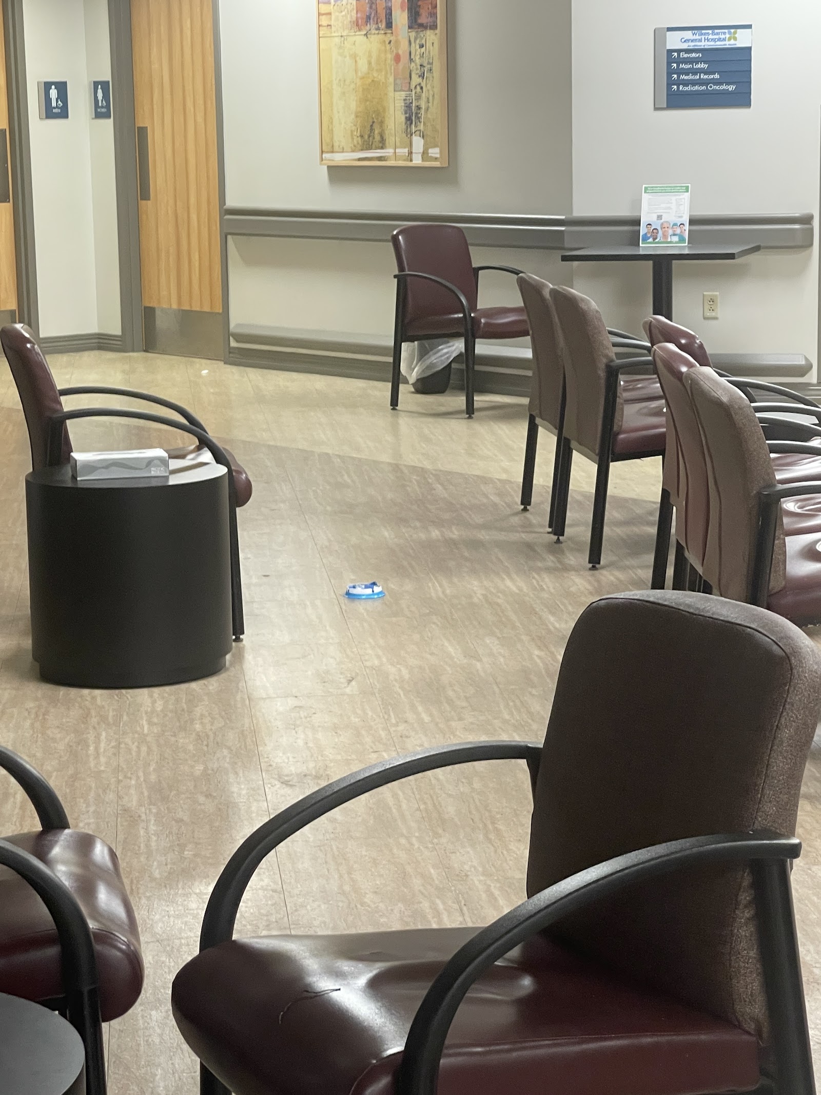 Interior common area with burgundy and tan patient chairs arranged around tables, wall signage, and yellow curtain partitions