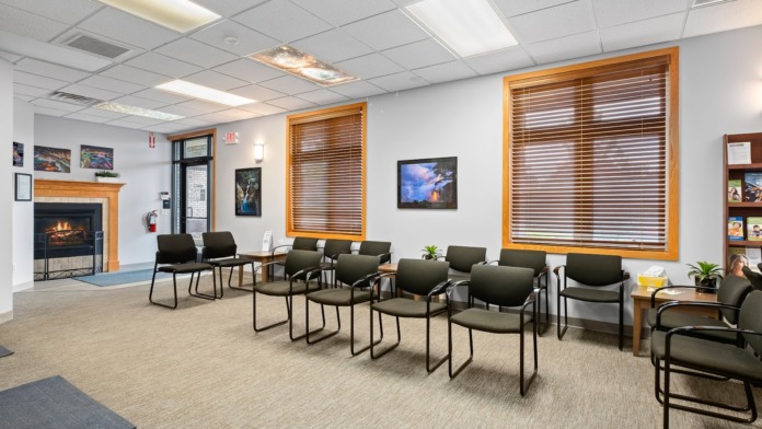 Interior seating area with multiple upholstered chairs, fireplace, large windows with blinds, and landscape artwork