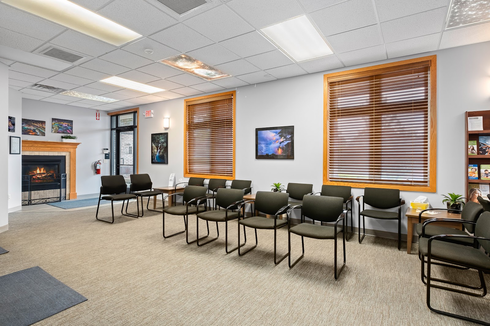 Interior seating area with multiple upholstered chairs, fireplace, large windows with blinds, and landscape artwork