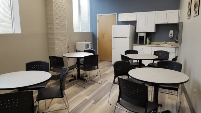 Interior dining space with multiple round tables, black chairs, kitchenette with white cabinets, and blue accent wall