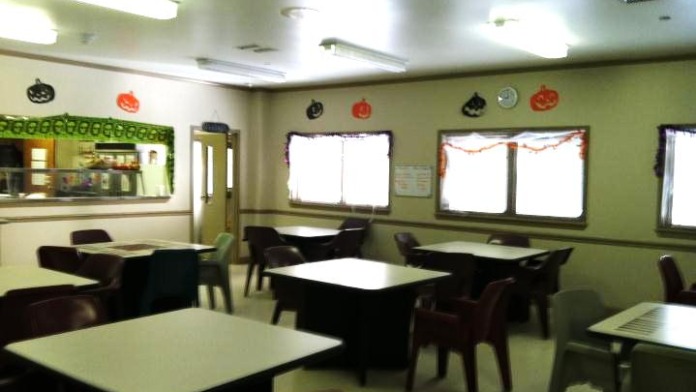 Interior dining area with multiple tables, chairs, service window, and green walls with decorative elements