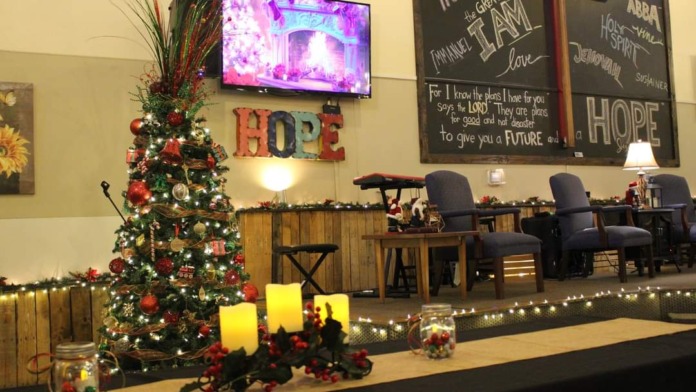 Interior community hall decorated with Christmas tree, lit candles, motivational signage, and screen displays