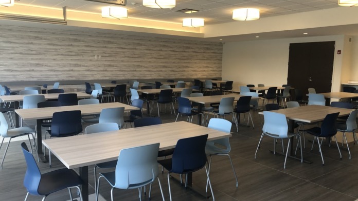 Interior dining and gathering area with multiple wooden tables, blue and black chairs, and accent wall