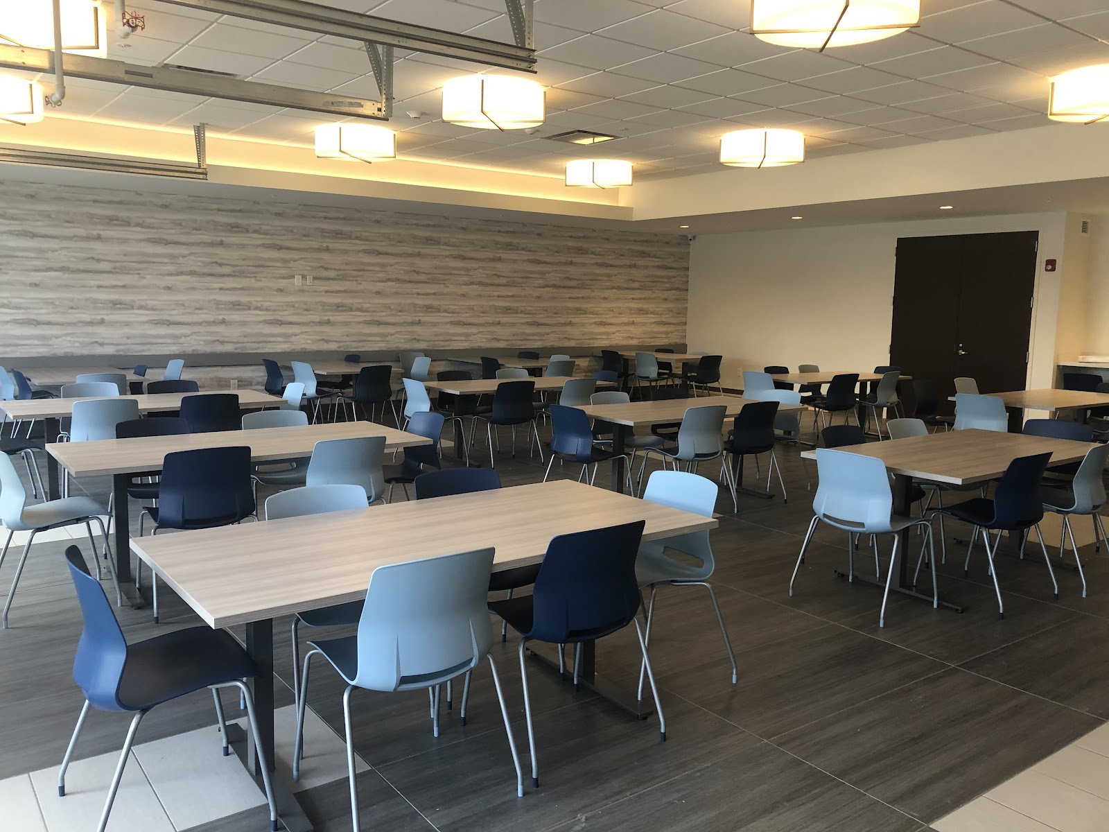 Interior dining and gathering area with multiple wooden tables, blue and black chairs, and accent wall