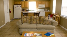Interior kitchen with yellow walls, wooden cabinets, refrigerator, stove, and dining table with magazines
