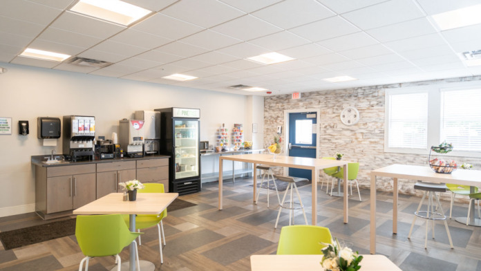 Interior communal kitchen and dining space with bright furniture, food preparation area, seating tables, and modern design