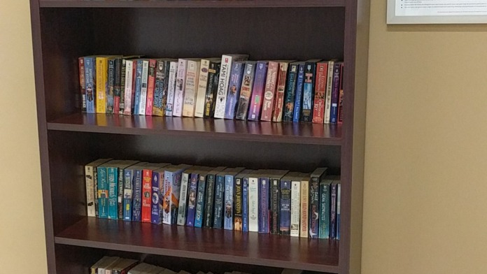 Interior bookshelf with DVDs and books, decorative flowers, and Take Read and Share signage