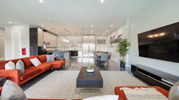 Interior open-concept living space with orange seating, kitchen visible, wall décor, mounted TV, and glass doors to outdoor area.