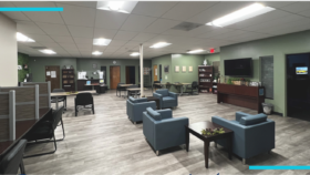 Interior community lounge with seating areas, reception desk, television, and administrative spaces in modern treatment facility