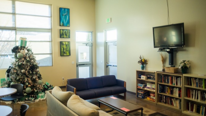 Interior lounge area with comfortable seating, TV, bookshelves, decorative artwork, and large windows with holiday decorations