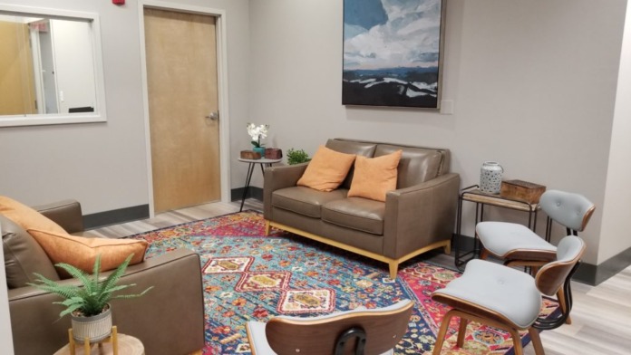 Interior lounge space with brown leather sofas, orange accent pillows, colorful area rug, and landscape artwork