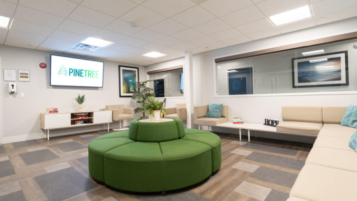 Interior lounge area with large circular green seating, beige sofas, television, and natural light from windows