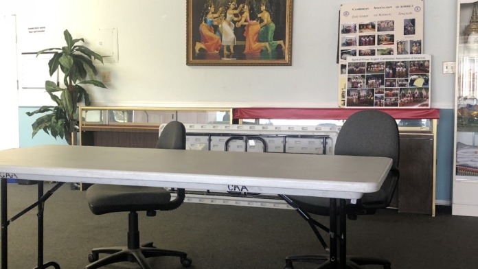 Interior meeting room with folding tables, office chairs, Cambodian artwork, and community event documentation on walls