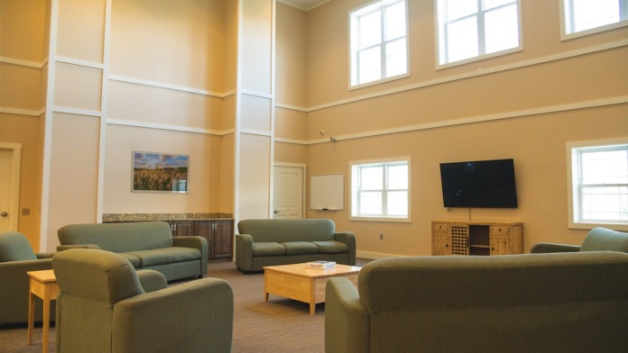 Interior common area with multiple upholstered seating, television, wooden furniture, windows, and comfortable gathering space
