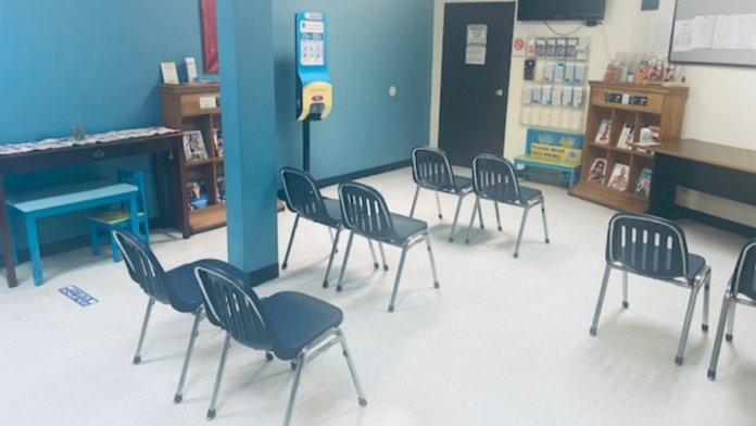 Interior group room with blue accent wall, wooden shelving with literature, black chairs, exit sign, and television.