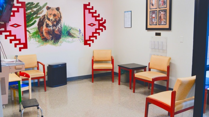 Interior community room with red-framed upholstered seating, Native American bear illustration, framed artwork, and clinical fixtures
