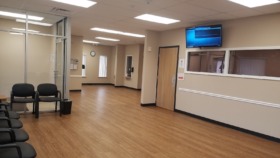 Interior waiting room with black chairs, wood flooring, wall-mounted television, and reception window