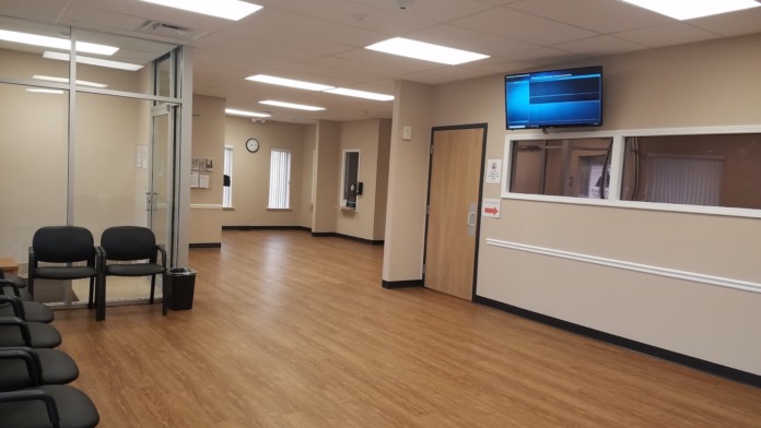 Interior waiting room with black chairs, wood flooring, wall-mounted television, and reception window