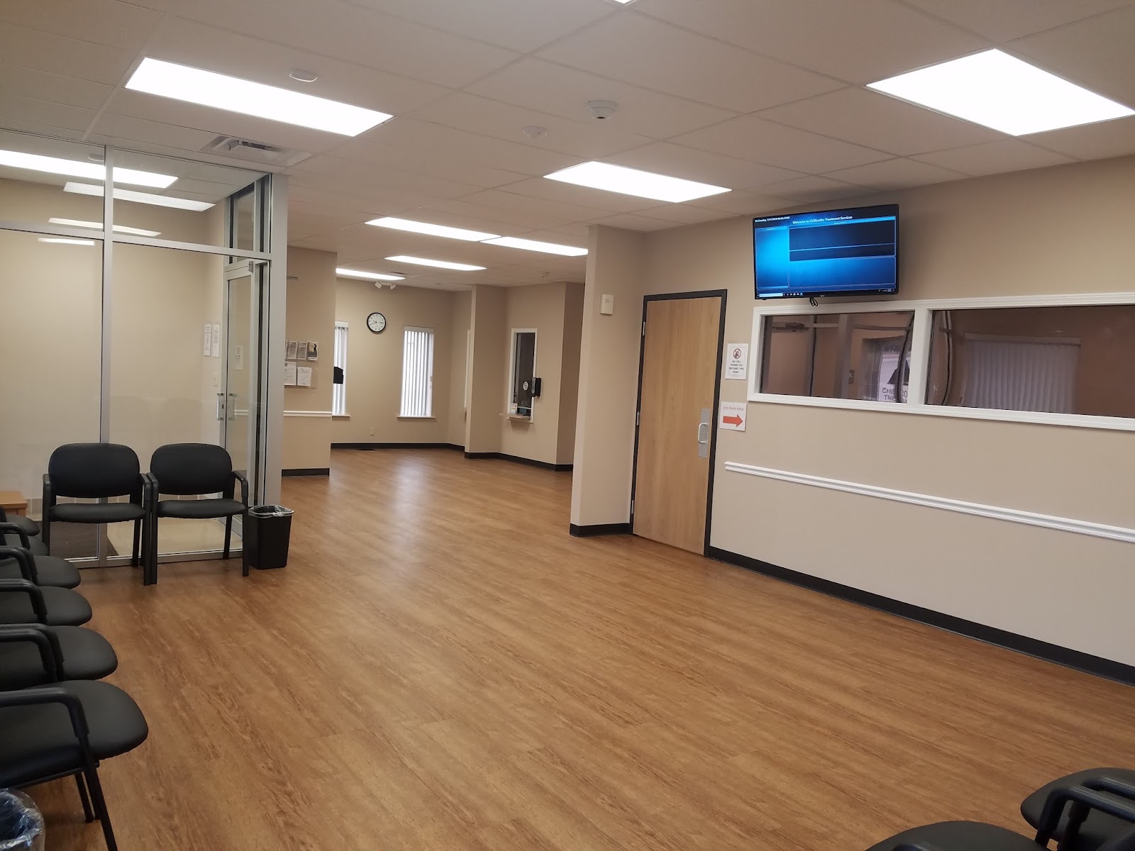 Interior waiting room with black chairs, wood flooring, wall-mounted television, and reception window