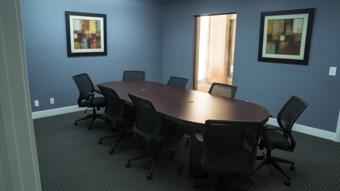 Interior conference room with long oval table, multiple black office chairs, artwork, and natural light from windows