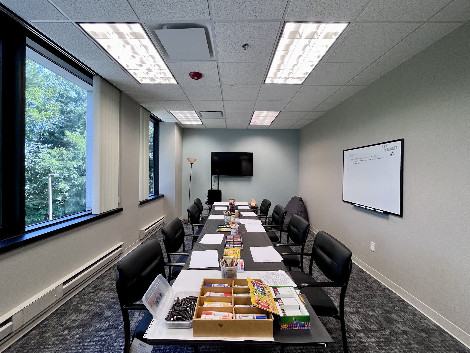Interior conference room with long table, black chairs, presentation screen, whiteboard, and large windows