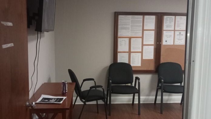 Interior consultation room with mounted television, small table, multiple black chairs, and informational bulletin board