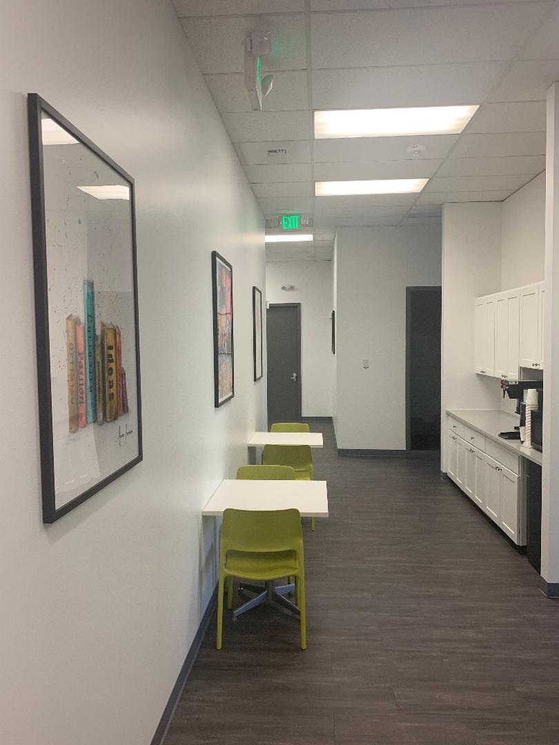 Interior hallway with white tables, green chairs, artwork, counter space, and modern cabinetry