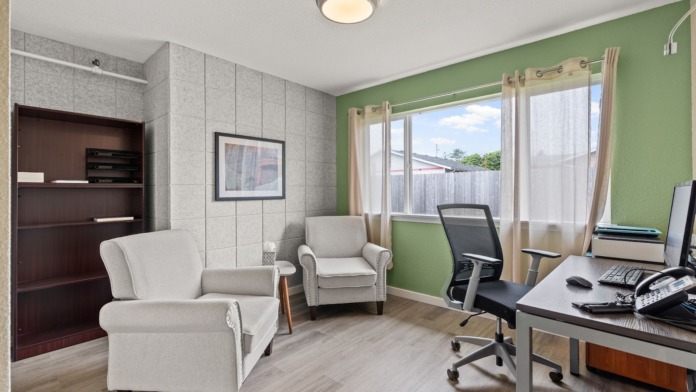 Interior counseling office with green accent wall, armchairs, desk with computer, wooden filing cabinet, and window
