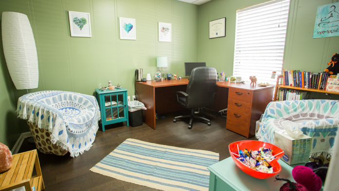 Interior office with green walls, wooden desk, office chair, bookshelves with books, decorative elements, and small seating area.
