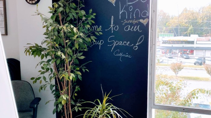 Interior office space with chalkboard wall, desk with coffee station, plants, and window with outside view