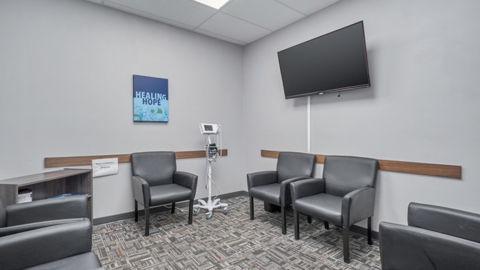 Interior group therapy room with gray chairs, wall-mounted television, wooden trim, and carpet flooring