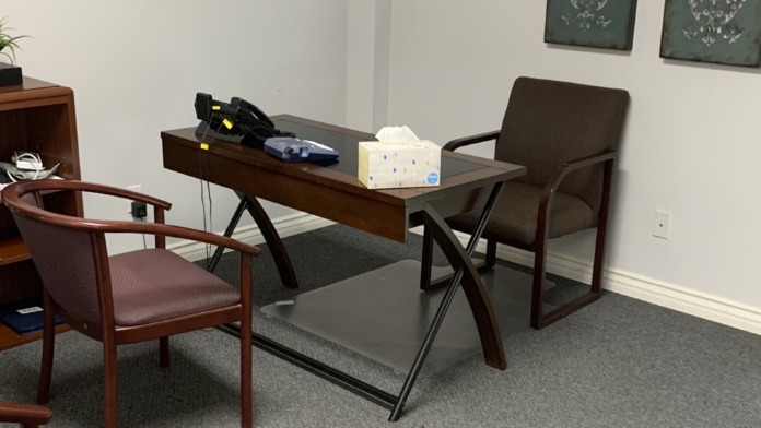Interior office space with wooden desk, upholstered chairs, wall art, and professional setup for individual counseling sessions