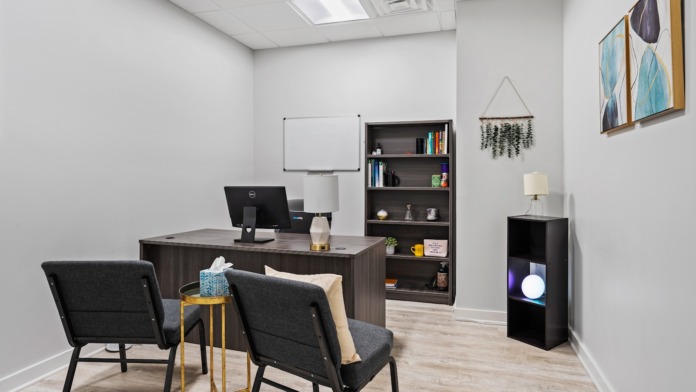Interior counseling office with desk, computer, bookshelves, motivational wall art, and professional seating