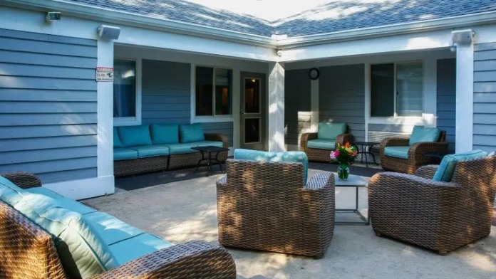 Exterior courtyard seating area with wicker furniture, blue cushions, and covered patio attached to building
