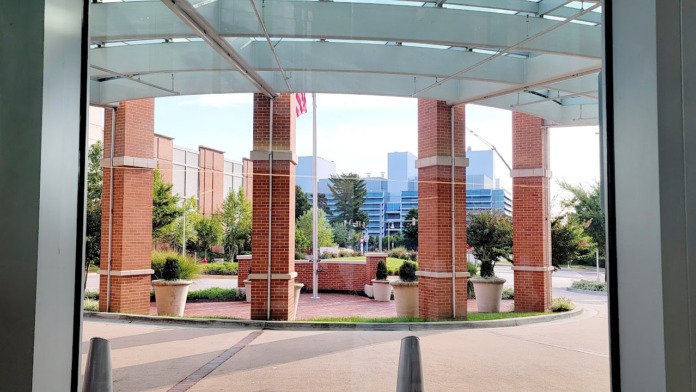 Exterior covered pavilion with glass walls, brick columns, brick patio flooring, landscaping, and distant city skyline view
