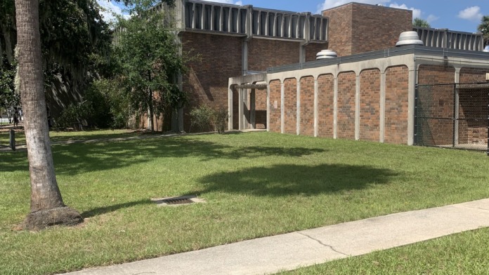 Exterior view showing brick building with covered pavilion structure and manicured lawn space